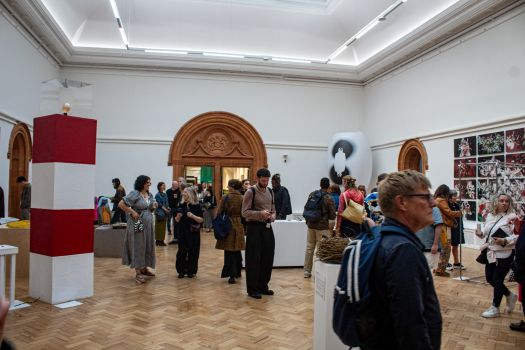 Visitors explore artworks displayed in a large gallery space at Manchester School of Art’s Degree Show, with sculptures, installations and wall-based pieces on view.